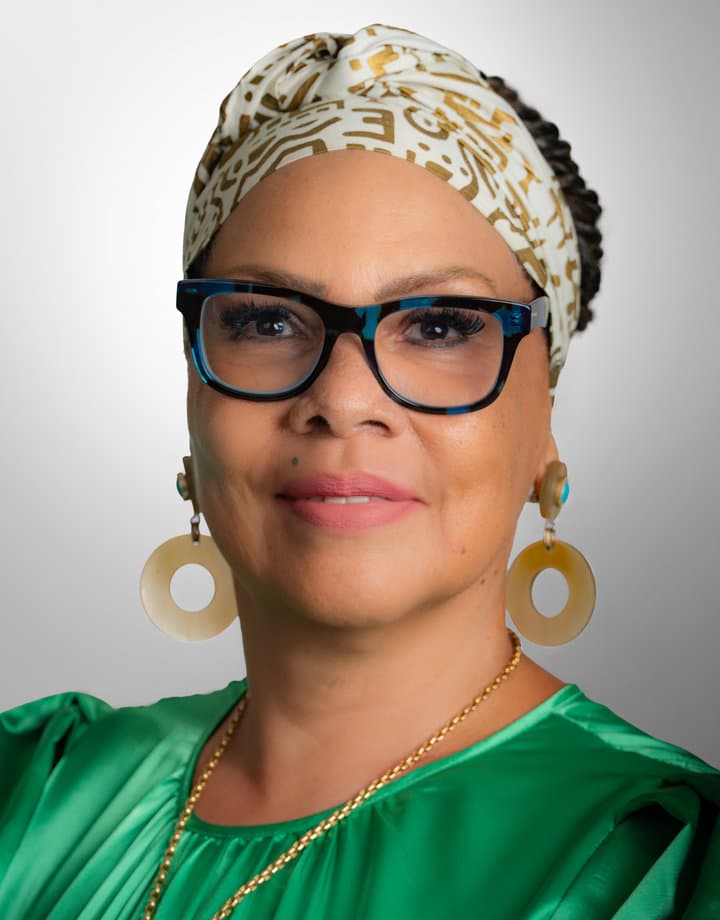 Dr. Sandra Clark-Glover in a patterned headwrap, blue glasses and an emerald blouse