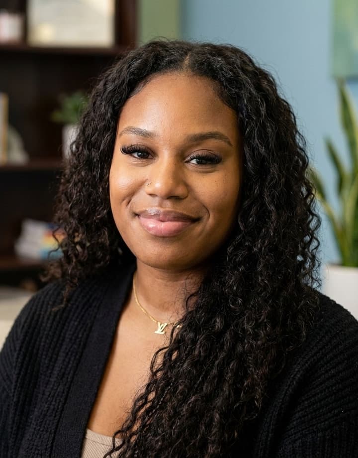 Taylar Keene with long curly hair, smiling in a black cardigan