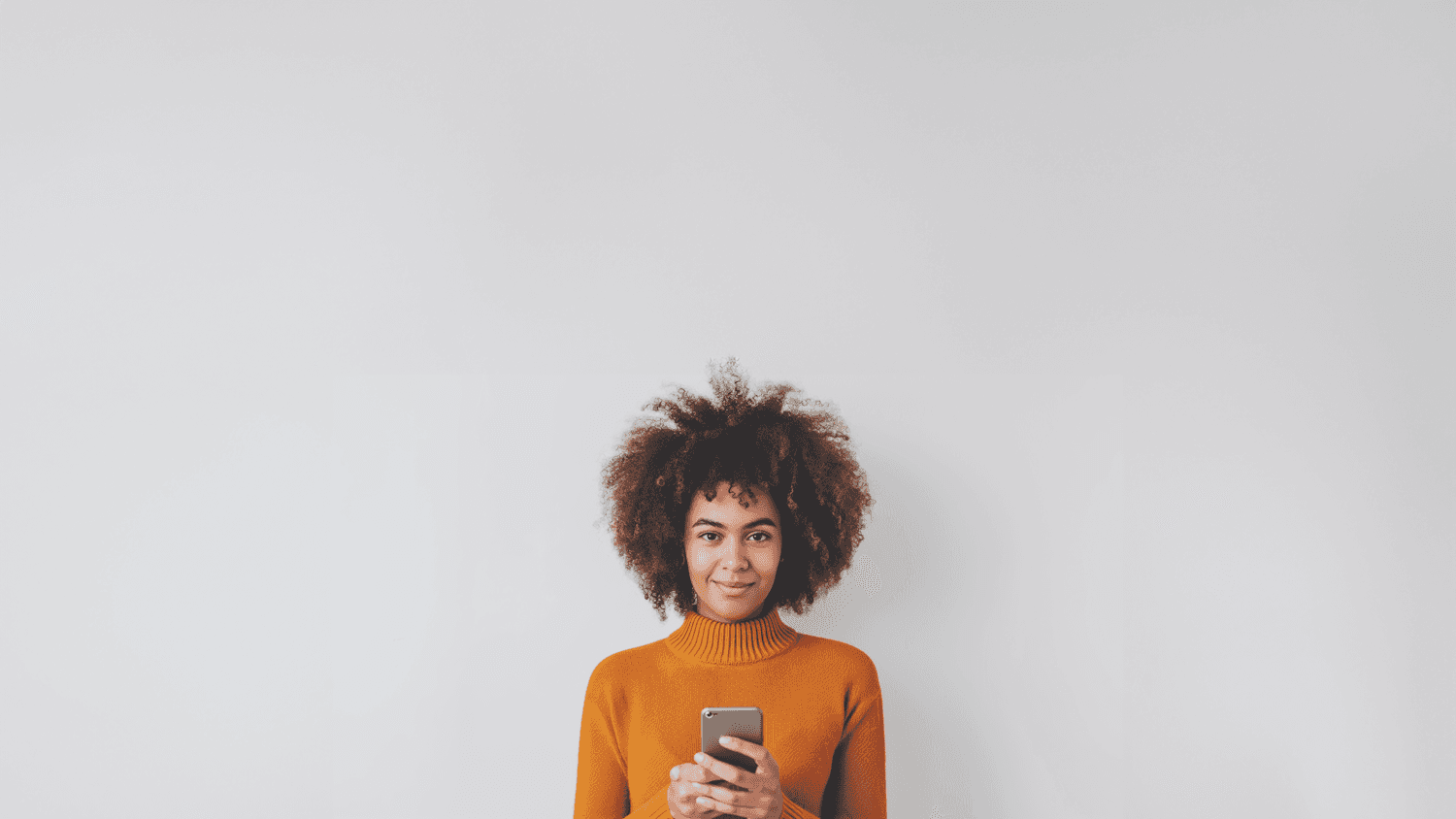 A smiling woman in an orange sweater holding her phone